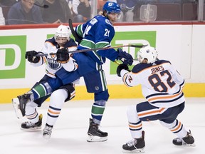 Edmonton Oilers defenseman Caleb Jones (82) and Edmonton Oilers defenseman Kris Russell (4) fight for control of the puck with Vancouver Canucks left wing Loui Eriksson (21) during second period NHL pre-season action at Rogers Arena in Vancouver, Tuesday, Sept, 18, 2018. THE CANADIAN PRESS/Jonathan Hayward