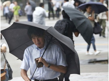 Pedestrians try to hold their umbrellas while struggling with strong winds in Yokohama, near Tokyo, Tuesday, Sept. 4, 2018.