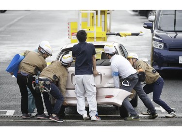 People move a car which was flown by strong wind caused by a powerful typhoon in Osaka, western Japan, Tuesday, Sept. 4, 2018.