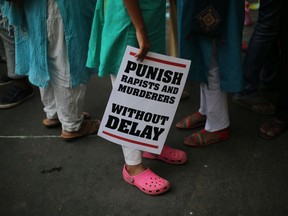 In this April 15, 2018 file photo, an Indian protester stands with a placard during a protest against two recently reported rape cases as they gather near the Indian parliament in New Delhi, India.
