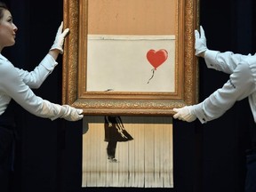 Sotheby's employees pose with the newly completed work by artist Banksy entitled "Love is in the Bin", a work that was created when the painting "Girl with Balloon" was passed through a shredder in a surprise intervention by the artist, at Sotheby's auction house in London on October 12, 2018, following the work's sale.
