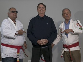 Brazilian presidential candidate Jair Bolsonaro smiles after receiving a honorary black belt from Jiu-Jitsu masters Robson Gracie, right, and Joao Carlos Austregesilo Athayde, in Rio de Janeiro, Brazil, Thursday, Oct. 25, 2018. Bolsonaro was awarded the honorary black belt out a respect for surviving a recent knife attack where he was wounded in the abdomen by a crazed attacker.