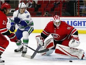 Hurricanes goalie Curtis McElhinney eyes the puck as teammate Justin Faulk and Canuck Bo Horvat look for the rebound.