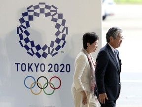 In this Aug. 24, 201, file photo, Tokyo Gov. Yuriko Koike, second from right, and Tsunekazu Takeda, president of the Japanese Olympic Committee, walk past the logo of the Tokyo 2020 Olympics during the Olympic flag arrival ceremony at Haneda international airport in Tokyo. The price tag keeps soaring for the 2020 Tokyo Olympics despite local organizers and the International Olympic Committee saying that spending is being cut.