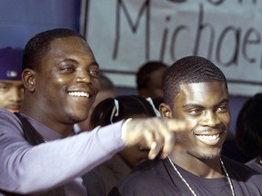 Michael Vick (right) and his father, Michael Boddie, smile as they acknowledge a friend in the audience during a news conference 11 January, 2001, in Newport News, Virginia. (WAYNE SCARBERRY/AFP/Getty Images)