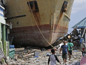 In this Thursday, Oct. 4, 2018, photo, men walk past Sabuk Nusantara 39 which was swept ashore by the tsunami in Wani village on the outskirt of Palu, Central Sulawesi, Indonesia. The crew of the hulking ferry dropped by the tsunami in front of a row of houses in an Indonesian village say the wave that drove them onto land was a towering 10-15 meters or higher and came just several minutes after a quake made the ship bounce like a basketball.