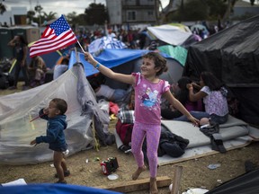 Seven-year-old Honduran migrant Genesis Belen Mejia Flores waves an American flag at U.S. border control helicopters flying overhead near the Benito Juarez Sports Center serving as a temporary shelter for Central American migrants, in Tijuana, Mexico, Saturday, Nov. 24, 2018.