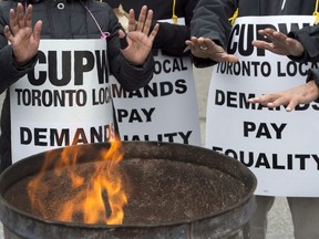 Striking Canada Post workers keep their hands warm as they picket at the South Central sorting facility in Toronto on Tuesday, November 13, 2018.