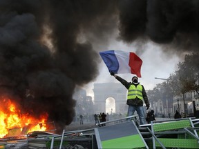 A demonstrator waves the French flag near a burning barricade on the Champs-Elysees avenue with the Arc de Triomphe in background, during a demonstration against rising fuel taxes in Paris, Saturday, Nov. 24, 2018.