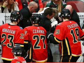 Calgary Flames centre Sean Monahan, centre Austin Czarnik and left wing Matthew Tkachuk look on as training staff treat head coach Bill Peters who was struck in the face with a puck during the second period of an NHL hockey game against the Arizona Coyotes, Sunday, Nov. 25, 2018, in Glendale, Ariz.