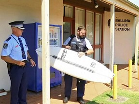In this Nov. 7, 2018, image made from video police holds a victim's surfboard at a police station in Ballina, Australia.  A man has used his surfboard to fend off a shark that bit him on his calf off an Australian beach two days after a fatal attack on the Great Barrier Reef.