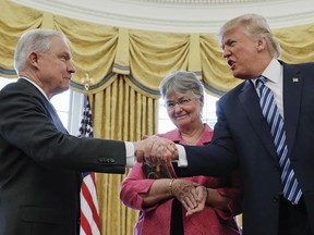 In this  Feb. 9, 2017 file photo, U.S. President Donald Trump shakes hands with Attorney General Jeff Sessions, accompanied by his wife Mary, after he was sworn-in by Vice President Mike Pence, in the Oval Office of the White House in Washington.