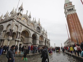 FILE - In this Thursday, Nov. 1, 2018 file photo, tourists walk in flooded St. Mark's Square in Venice, Italy. The mayor of Venice says Italy's new budget law includes a measure allowing the lagoon city to charge all visitors for accessing the historic center -- not just those sleeping in hotels or other accommodations. Mayor Luigi Brugnaro announced on Twitter late Sunday, Dec. 30, 2018 that the tax will ''allow us to manage the city better and to keep it clean,'' and ''above all allow Venetians to live with more decorum.'' The city council will determine the amount of the tax and collection mode.