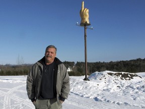 Ted Pelkey stands in front of a wooden sculpture on his front lawn on Thursday, Dec. 13, 2018, in Westford, Vt. Pelkey, who is in an ongoing dispute with the town over plans to move his truck repair and recycling business to his property, paid to have the sculpture created to send a message to the town.