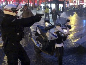In this image made from video taken on Saturday, Dec. 22, 2018, a French policeman, at left, brandishes a gun at yellow vest protesters during clashes on the Champs Elysees in Paris. (Clement Lanot via AP)