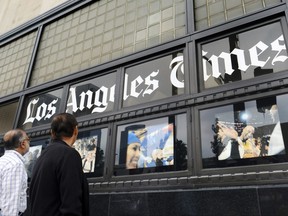 In this May 16, 2016, file photo, pedestrians look at news photos posted outside the Los Angeles Times building in downtown Los Angeles. (AP Photo/Richard Vogel, File)
