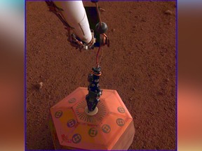 This photo provided by NASA Jet Propulsion Laboratory, shows the new Mars lander placing a quake monitor on the planet’s dusty red surface.