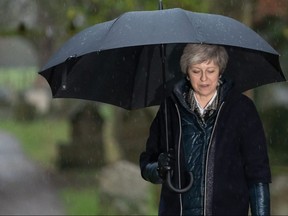 Britain's Prime Minister Theresa May shelters from the rain under an umbrella after attending a church service near her Maidenhead constituency, west of London on Sunday, Dec. 9, 2018.
