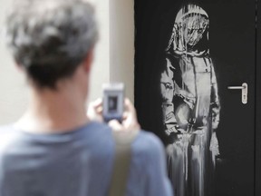 In this file photo taken on June 25, 2018, a man takes a photograph of an artwork by street artist Banksy in Paris on a side street to the Bataclan concert hall where a terrorist attack killed 90 people on Novembre 13, 2015. - The artwork by street artist Banksy on a side street to the Bataclan concert hall was stolen in Paris on January 26, 2019.