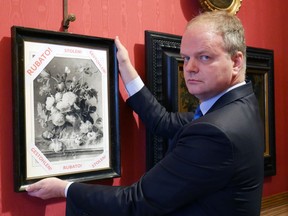 In this photo made available on Jan. 1, 2019 by the Uffizi gallery press office, Eike Schmidt, director of the Uffizi Gallery, poses for a photo as he holds onto a copy of a still-life "Vase of Flowers", by Dutch artist Jan van Huysum, with writing in red reading "stolen", inside the Uffizi gallery, in Florence, Italy. (Uffizi Gallery press office via AP)