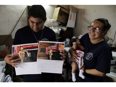 In this Jan. 12, 2019 photo, firefighter Fatima Olmedo, right, holds her two-month-old baby Samara as her husband Rodrigo Gimenez holds calendar pages with their photos posing nude, in Asuncion, Paraguay.