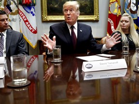 President Donald Trump is reflected in the table as he gestures while speaking during a healthcare roundtable in the Roosevelt Room of the White House, Wednesday, Jan. 23, 2019, in Washington. With the president are David Silverstein, of Denver, left, and Jamesia Shutt, of Aurora, Colo., right.