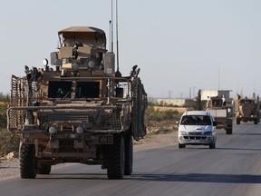 In this March 31, 2018 file photo, a convoy of U.S. troops drive along a road leading to the front line with Turkish-backed fighters, in Manbij, Syria.