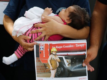 In this Jan. 12, 2019 photo, firefighter Fatima Olmedo holds her two-month-old baby Samara as her husband holds a calendar page with a photo Olmedo posing nude while pregnant, in Asuncion, Paraguay.