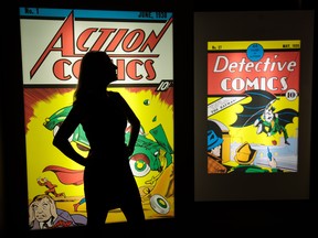 An employee poses in front illuminated displays of the first comics to feature Superman and Batman at the DC Comics Exhibition: Dawn Of Super Heroes at the O2 Arena on Feb. 22, 2018 in London, England. (Jack Taylor/Getty Images)