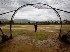 In this March 10, 2015 photo, Seattle Mariners ground worker Carlos Galindez sprays water on the field after a training session at the Seattle Mariners' baseball academy in Aguirre, Venezuela. (AP Photo/Fernando Llano)