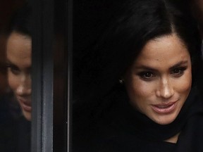 Meghan, Duchess of Sussex is reflected in a glass door as she leaves after a visit with her husband Britain's Prince Harry to the Old Vic Theatre in Bristol, England, Friday, Feb. 1, 2019.