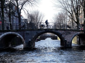 A cyclist pedals over a bridge over the Leidsegracht canal in Amsterdam, Thursday, Feb. 7, 2019. (AP Photo/Michael Corder)
