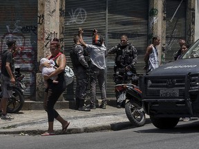 A woman carries a baby as she walks past police searching several men, during an operation targeting drug traffickers in the Santa Teresa neighborhood of Rio de Janeiro, Friday, Feb. 8, 2019. (AP Photo/Carson Gardiner)