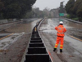 In this Saturday, Feb. 2, 2019, photo released by Santa Barbara County Fire, a Caltrans worker stands in the northbound U.S 101, where the nearby Romero Creek has overflowed and flooded in the Montecito area of Santa Barbara County, Calif. (Mike Eliason/Santa Barbara County Fire via AP)