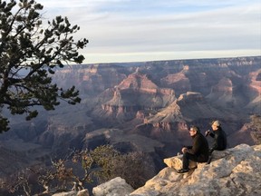 Tourists sit on the edge of the Grand Canyon — a must-see site for Arizona visitors.