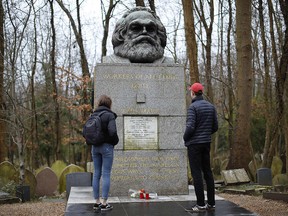Visitors look at the tomb of German revolutionary philosopher Karl Marx, a Grade I-listed monument, with the marble plaque on the front showing damage from recent vandalism in Highgate Cemetery in north London on Feb. 5, 2019.