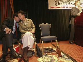 In this Feb. 19, 2004, file photo, James Fang, left, talks with his mother, Florence Fang, as president and publisher of The San Francisco Examiner and Independent newspapers Scott McKibben, second from right, announces The Anschutz Co. purchasing the newspapers from the Fang family at the Ritz-Carlton in San Francisco. A San Francisco Bay Area town is suing Florence Fang, the owner of the quirky Flintstone House, alleging she violated local codes when she put dinosaur sculptures in the backyard and made other landscaping changes that caused local officials to declare it a public nuisance. The town of Hillsborough filed a complaint this week against Fang, the media mogul who purchased the orange-and-purple, bulbous-shaped house in 2017.