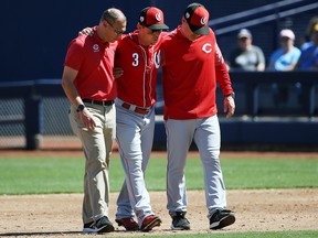 Cincinnati Reds second baseman Scooter Gennett leaves the baseball game with the help of manager David Bell, right, and head athletic trainer Steve Baumann, left, after he was injured in the second inning of a spring training baseball game against the Milwaukee Brewers, Friday, March 22, 2019, in Phoenix.