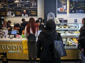 Customers wait in line for service at Godiva's new cafe in New York, Tuesday April 16, 2019. (AP Photo/Bebeto Matthews)