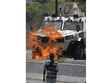 An opposition demonstrator looks at an armoured vehicle in flames during clashes with soldiers loyal to Venezuelan President Nicolas Maduro after troops joined opposition leader Juan Guaido in his campaign to oust Maduro's government, in the surroundings of La Carlota military base in Caracas on April 30, 2019.