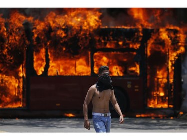 An anti-government protester walks near a bus that was set on fire by opponents of Venezuela's President Nicolas Maduro during clashes between rebel and loyalist soldiers in Caracas, Venezuela, Tuesday, April 30, 2019.