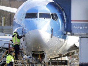 In this March 13, 2019, file photo a worker stands on a platform near a Boeing 737 MAX 8 airplane being built for TUI Group at Boeing Co.'s Renton Assembly Plant in Renton, Wash. Boeing is cutting production of its grounded Max airliner this month to focus on fixing flight-control software and getting the planes back in the air. The company said Friday, April 5, that starting in mid-April it will cut production of the 737 Max from 52 to 42 planes per month.