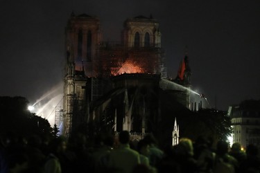 People watch Notre Dame cathedral burning in Paris, Monday, April 15, 2019. A catastrophic fire engulfed the upper reaches of Paris' soaring Notre Dame Cathedral as it was undergoing renovations Monday, threatening one of the greatest architectural treasures of the Western world as tourists and Parisians looked on aghast from the streets below. (AP Photo/Christophe Ena)