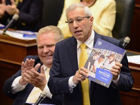 Flanked by Premier Doug Ford, left, Ontario Finance Minister Vic Fedeli presents the 2019 budget to the legislature on Thursday.