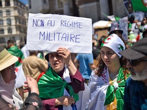 A flag-clad Algerian woman raises a placard on May 10, 2019, as demonstrators continue their weekly protests in the capital Algiers to demand the overthrow of the "system". The placard reads in Arabic: "No to the military regime."