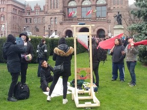 May Day protesters poses with signs, Communist flags and guillotine at Queen's Park on Wednesday, May 1 2019.