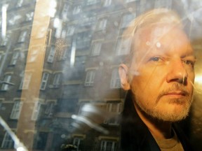 In this Wednesday May 1, 2019 file photo, buildings are reflected in the window as WikiLeaks founder Julian Assange is taken from court, where he appeared on charges of jumping British bail seven years ago, in London.