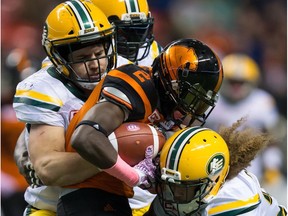 Edmonton Eskimos linebacker Adam Konar, left, and Aaron Grymes, right, tackle B.C. Lions ball carrier Chris Rainey in Vancouver on Oct. 21, 2017.