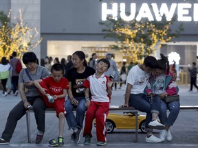 In this photo taken Monday, May 20, 2019, residents enjoy a cool evening near a Huawei store in Beijing. The Trump administration's sanctions against Huawei have begun to bite even though their dimensions remain unclear.