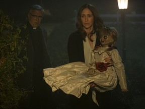 Vera Farmiga, right, carries the titular devil-doll in "Annabelle Comes Home," as Steve Coulter, left, playing a priest, prepares to sprinkle the cursed toy with holy water. (Justin Lubin/Warner Bros. Pictures)